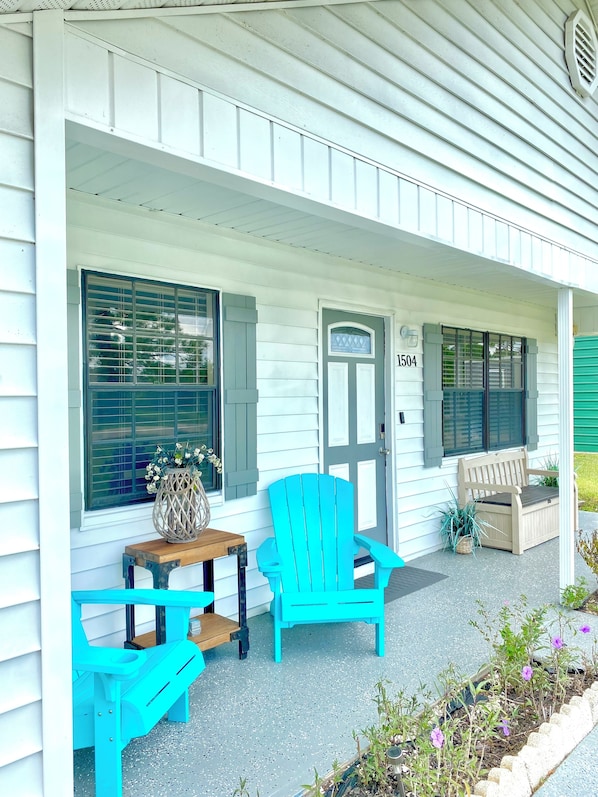 A porch with two turquoise Adirondack chairs, a wooden table, and a potted plant.