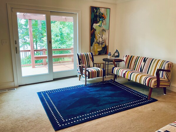 A living room with a sofa, two chairs, a rug, a painting, and a sliding glass door leading to a balcony.
