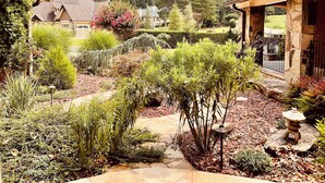 Um jardim bem cuidado com um caminho de pedra, diversos arbustos e uma pequena árvore.
