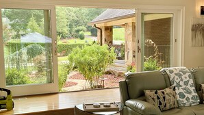 Uma sala de estar com um sofá verde, uma mesa de centro de vidro e vista para um jardim através de grandes portas de correr.