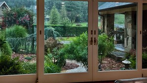 Visão através de portas de vidro que dão para um jardim com diversas plantas e um caminho de pedra.