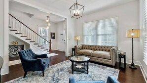 Una sala de estar con una escalera, un sofá color beige, un sillón azul, una mesa de centro y una lámpara de pie.