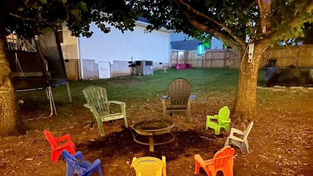 Un jardin avec un foyer, plusieurs chaises en plastique et un arbre.