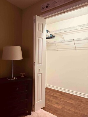 Um quarto com porta fechada, um penteou com abajur e um guarda-roupa branco com prateleiras.