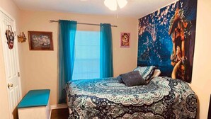 Une chambre à coucher avec un grand lit, un banc, une fenêtre avec des rideaux et un mur orné d’un tableau.