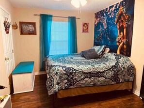 Une chambre à coucher avec un grand lit, un banc, une fenêtre avec des rideaux et un mur orné d’un tableau.