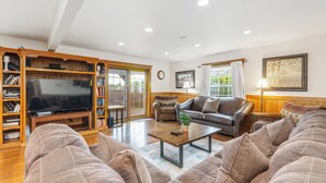 A spacious living room with a large flat-screen TV, leather sofas, a coffee table, and a bookshelf. - Spacious 9BR Family Retreat w/Indoor Heated Pool! (Amsterdam)