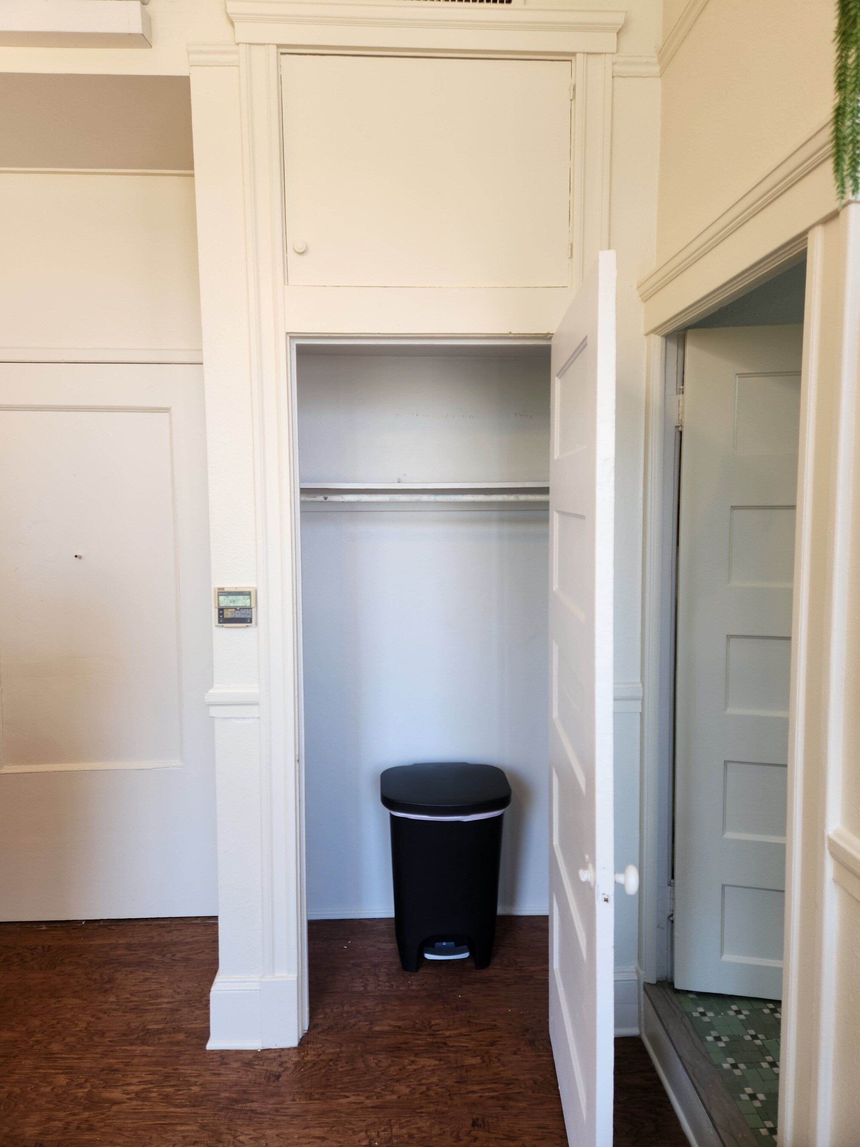 A hallway with a black trash bin, a white door, and a green and white tiled area.