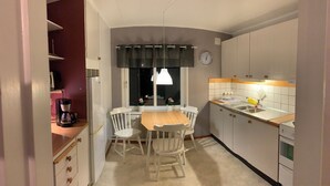 A compact kitchen with a dining table, chairs, a coffee maker, a refrigerator, a clock, and a window with curtains. - 4 Bed Apartment with balcony in Karlskrona (Karlskrona)