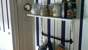 A kitchen with striped wallpaper, a white door, and shelves holding jars, bottles, and kitchen utensils.