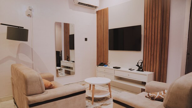 A modern living room with two sofas, a small round table, a TV mounted on the wall, and a mirror. - Sapphire Residences by Crystal (Lagos)