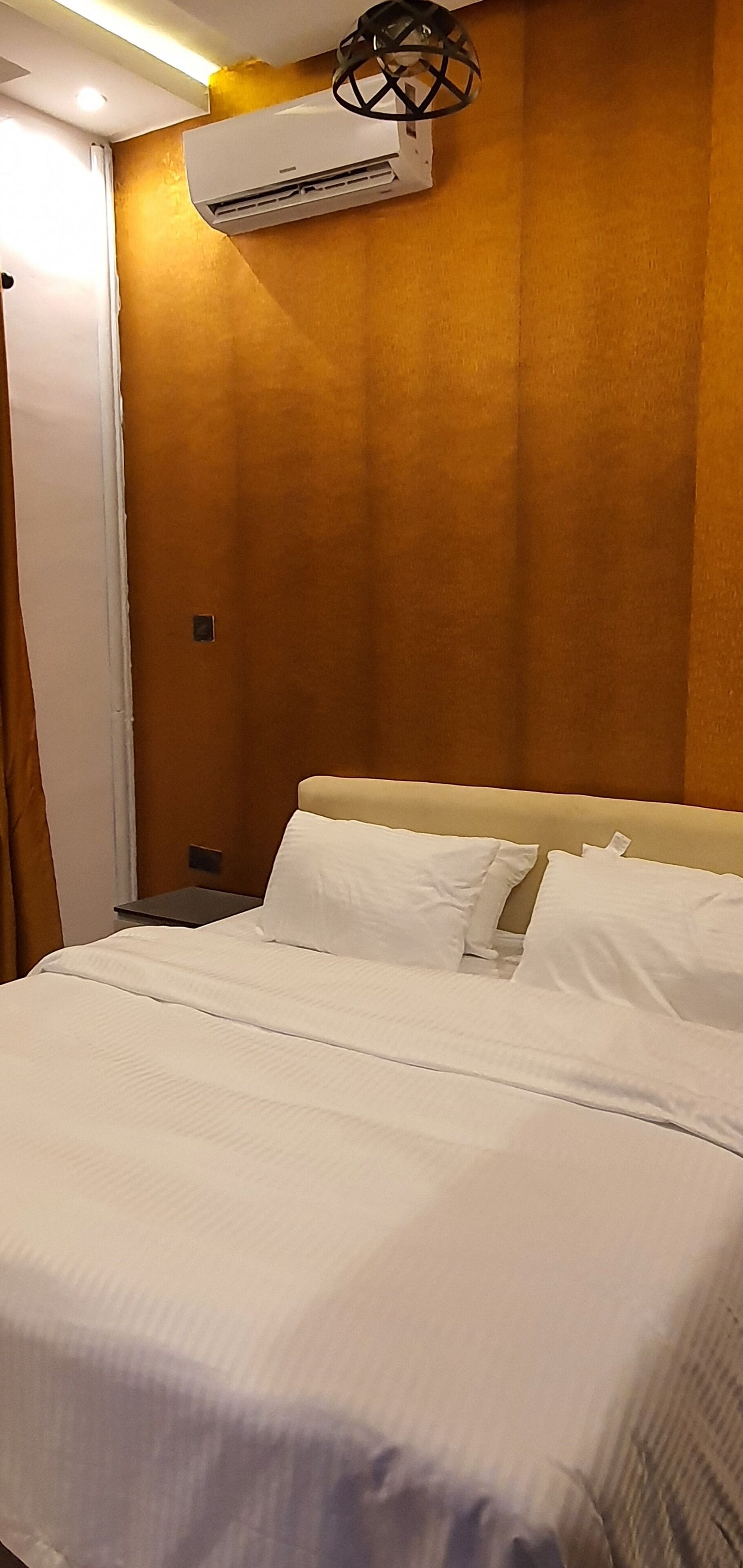 Ein Hotelzimmer mit Bett, weißer Bettwäsche, einer Klimaanlage, einem Nachttisch und einer Lampe.