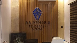 A reception desk with a wooden finish, a logo with a blue diamond, and an air conditioning unit above it. - Sapphire Residences by Crystal (Lagos)