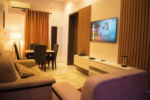 A modern living room with a sofa, armchair, and a TV mounted on the wall. - Sapphire Residences by Crystal (Lagos)