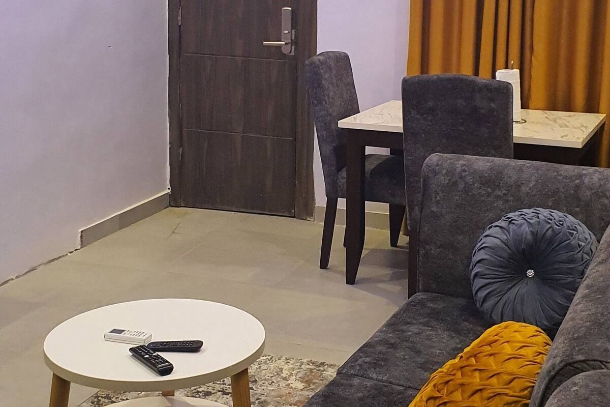 A living room with a sofa, a small round table, a chair, and a dining table.