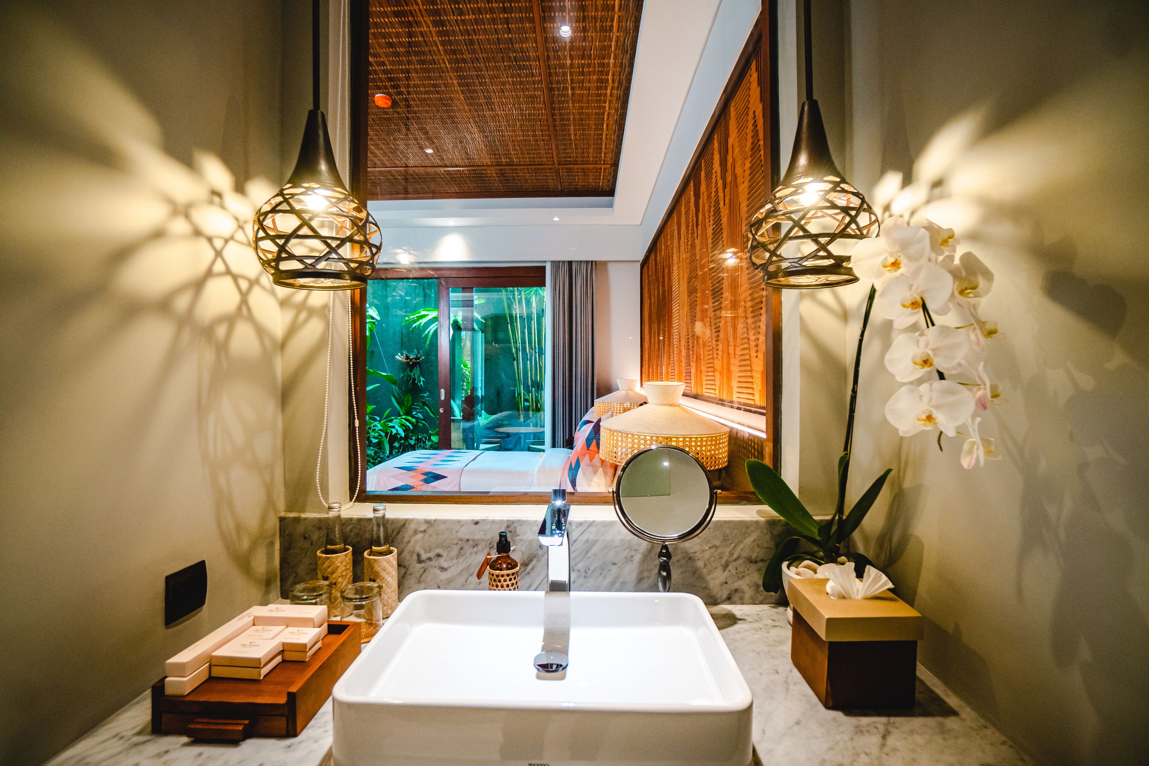 A bathroom with a large window, a sink, two pendant lights, a mirror, and a potted orchid.
