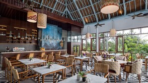 A spacious restaurant with high ceilings, large windows, and a variety of seating arrangements including tables and chairs. - The Hava Ubud A Pramana Experience (Ubud)