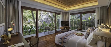 A spacious bedroom with a large bed, a TV, and a dining area with a view of the garden.
