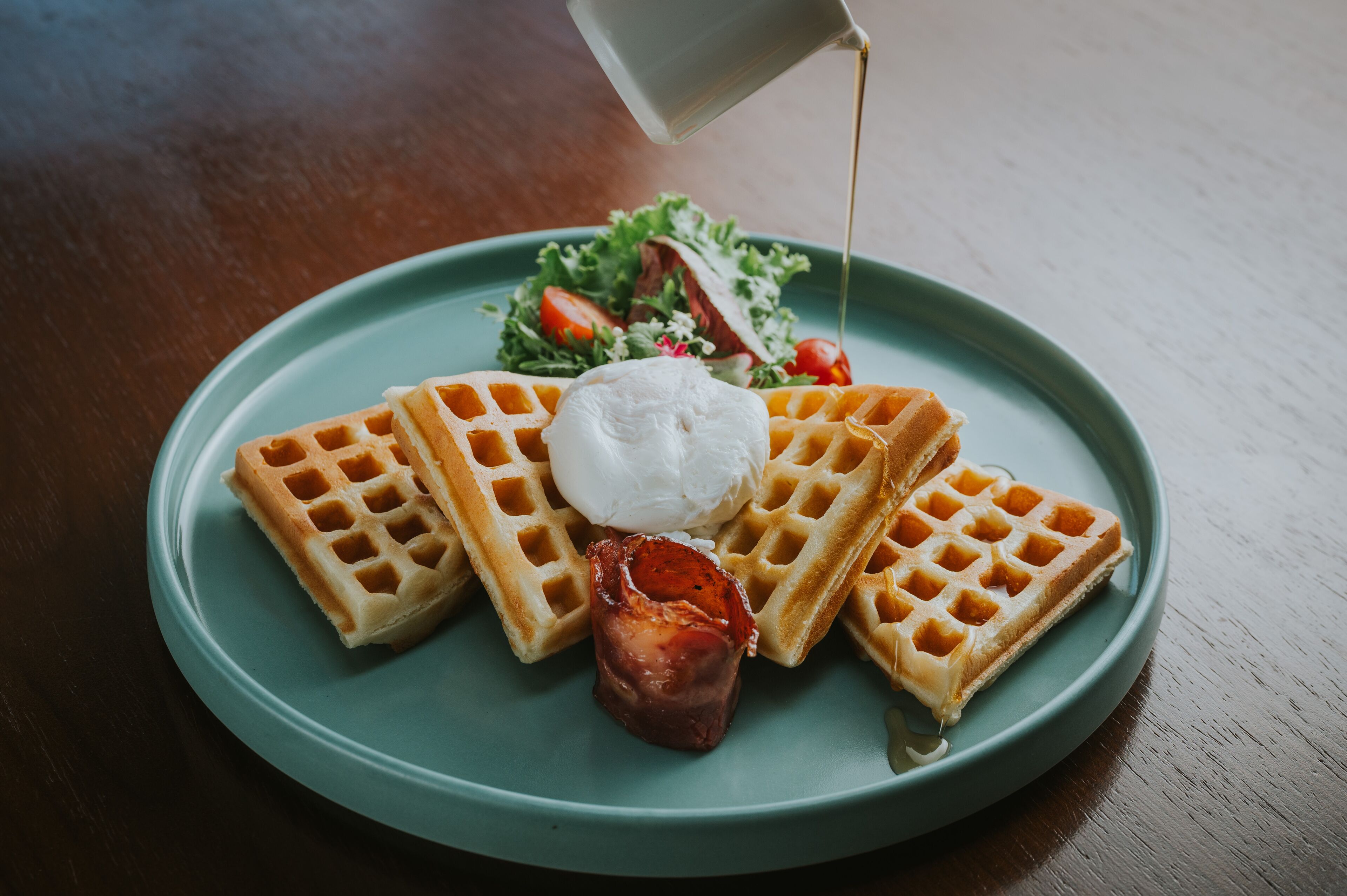 A plate with waffles, a dollop of cream, and a piece of bacon.