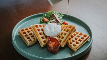 Un plato con waffles, crema batida y un trozo de tocino.