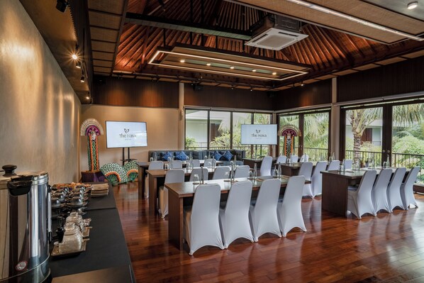 A conference room with multiple tables and chairs, large windows with a view of greenery, and a buffet area with coffee dispensers. - The Hava Ubud A Pramana Experience (Ubud)