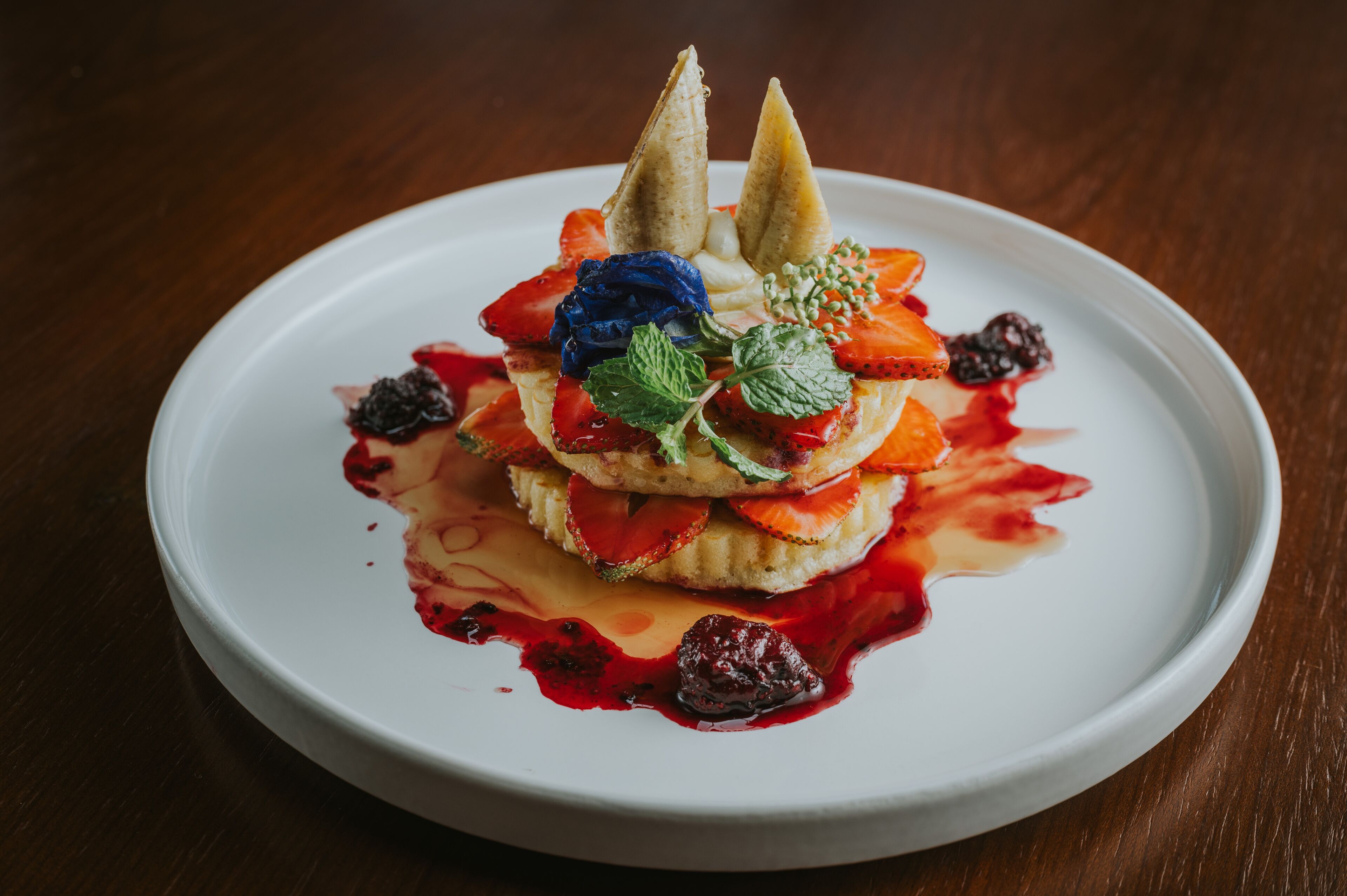 A dessert on a white plate with strawberries, mint, and a berry sauce.