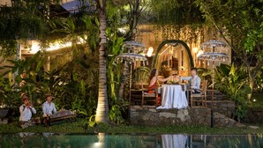 An outdoor dining area with a pool, surrounded by lush greenery and stone structures. - The Hava Ubud A Pramana Experience (Ubud)