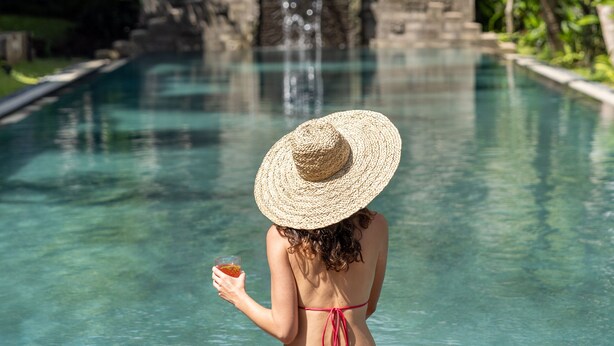 A woman in a bikini and straw hat sitting by a pool with a waterfall in the background. - The Hava Ubud A Pramana Experience (Ubud)