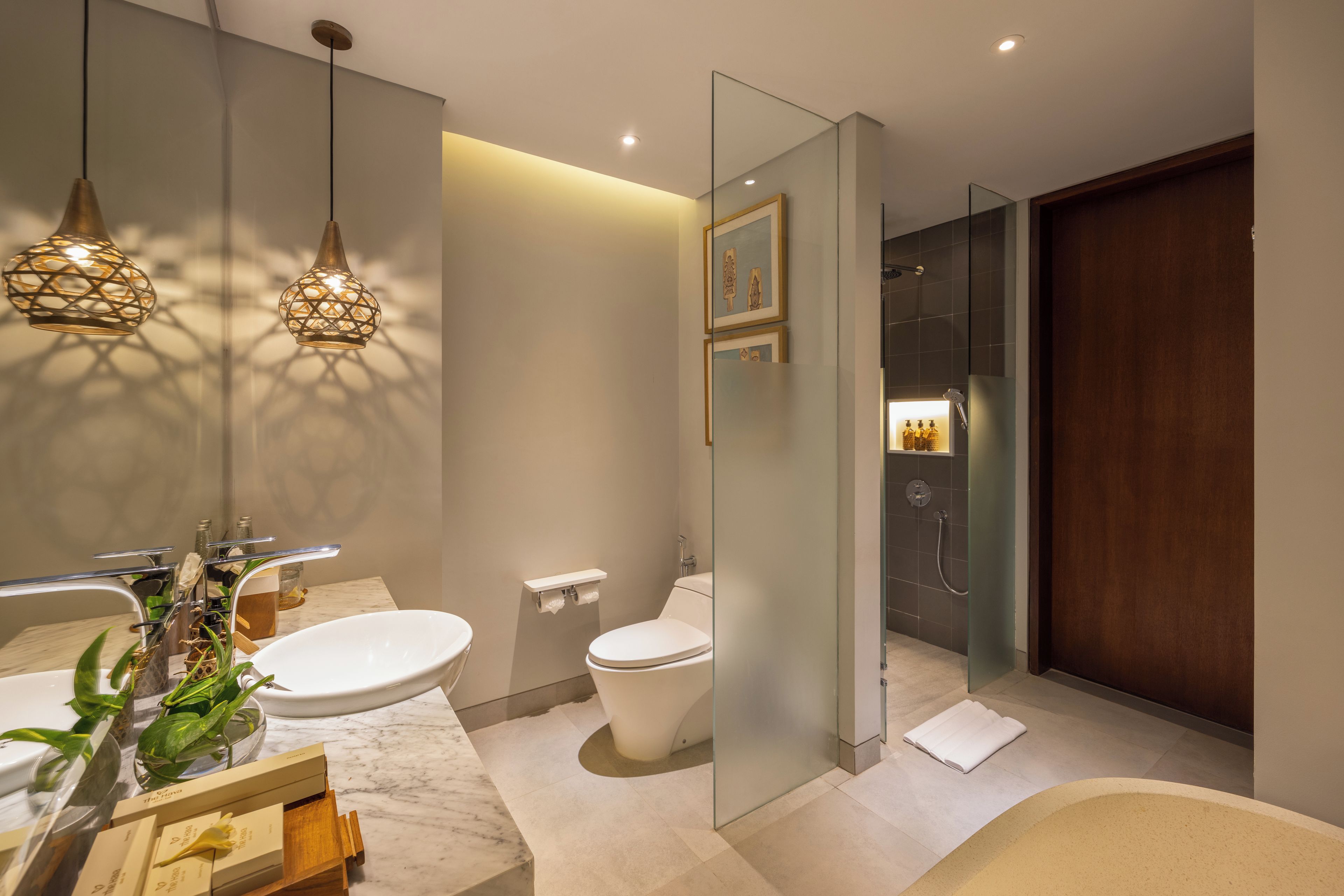 Une salle de bain moderne avec un comptoir en marbre, des toilettes blanches, une douche en verre et des luminaires suspendus.
