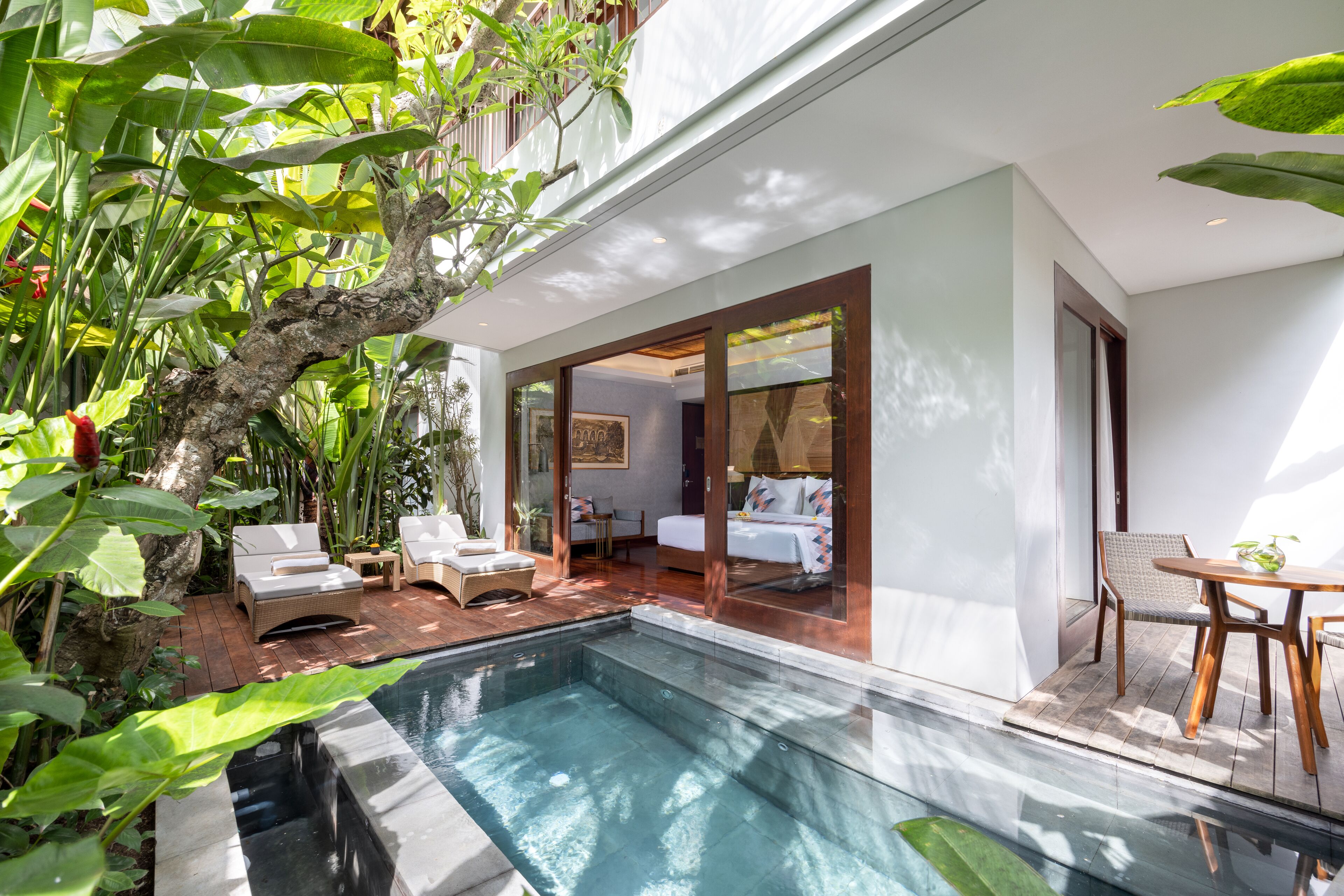 A modern outdoor pool area with lounge chairs, a hot tub, and a bedroom with a large window.
