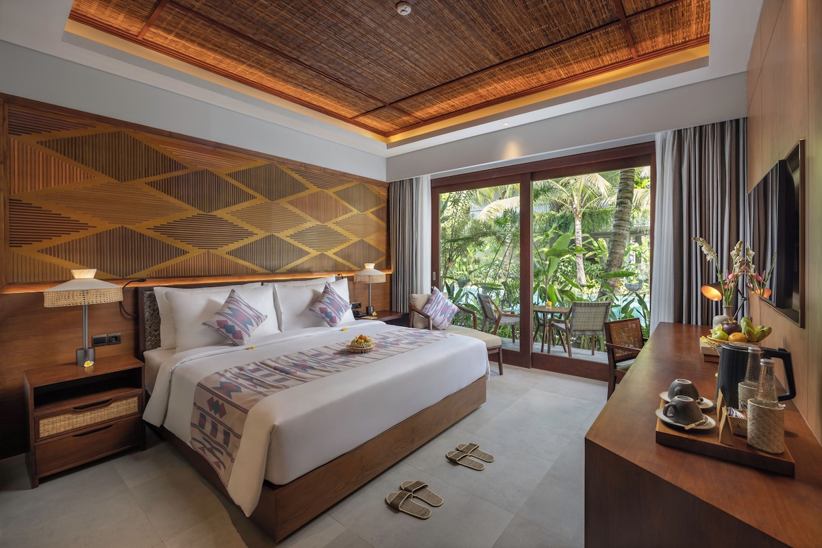 A modern hotel room with a large bed, a desk with a view, and a ceiling with a geometric pattern.