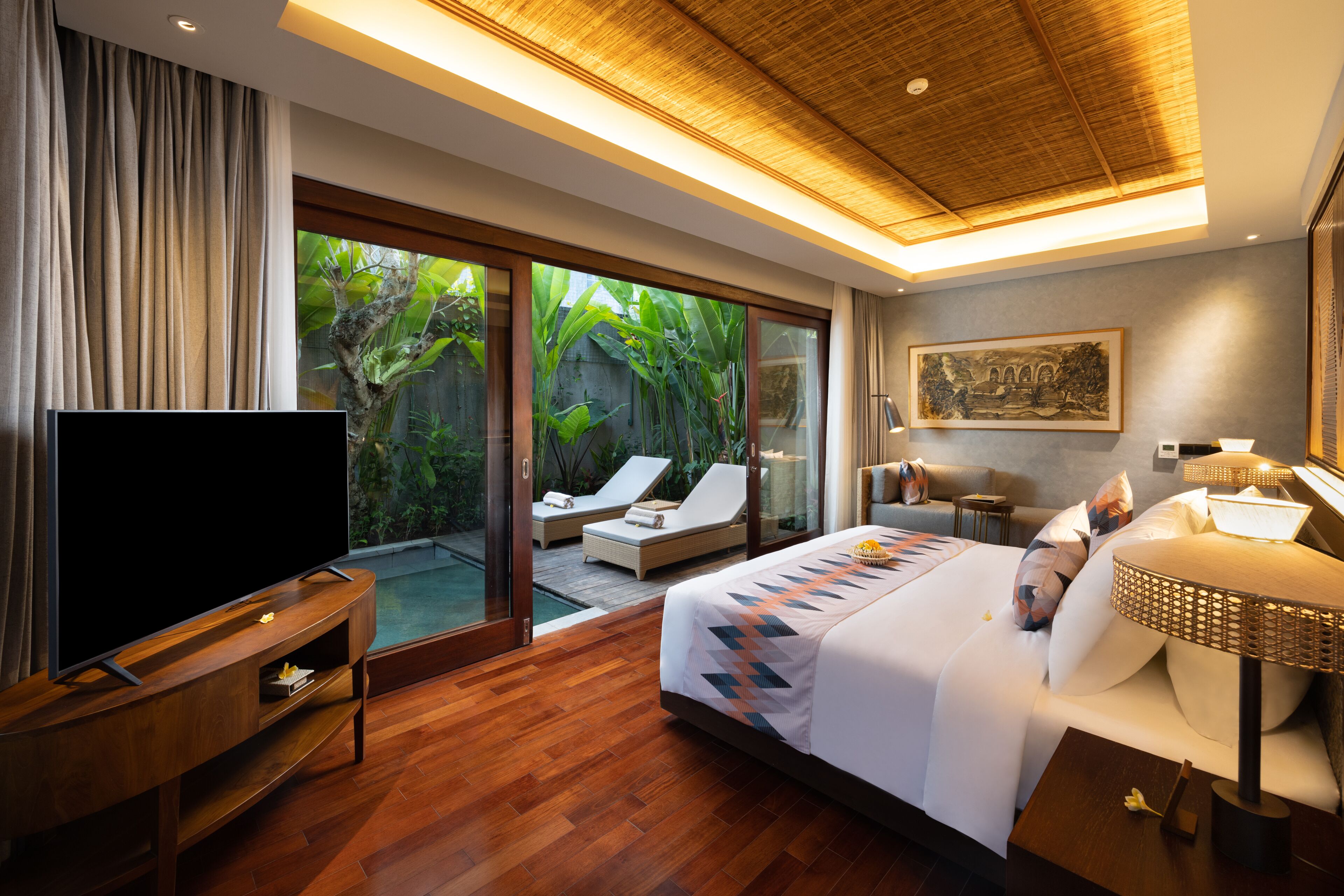 Une chambre d’hôtel moderne dotée d’un grand lit, d’une télévision, d’une porte vitrée donnant sur une piscine et offrant une vue sur une végétation luxuriante.
