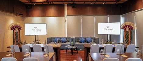 A conference room with a wooden ceiling, two large screens displaying 'The Hava', a grey sofa with blue patterned cushions, and a round table in the center.