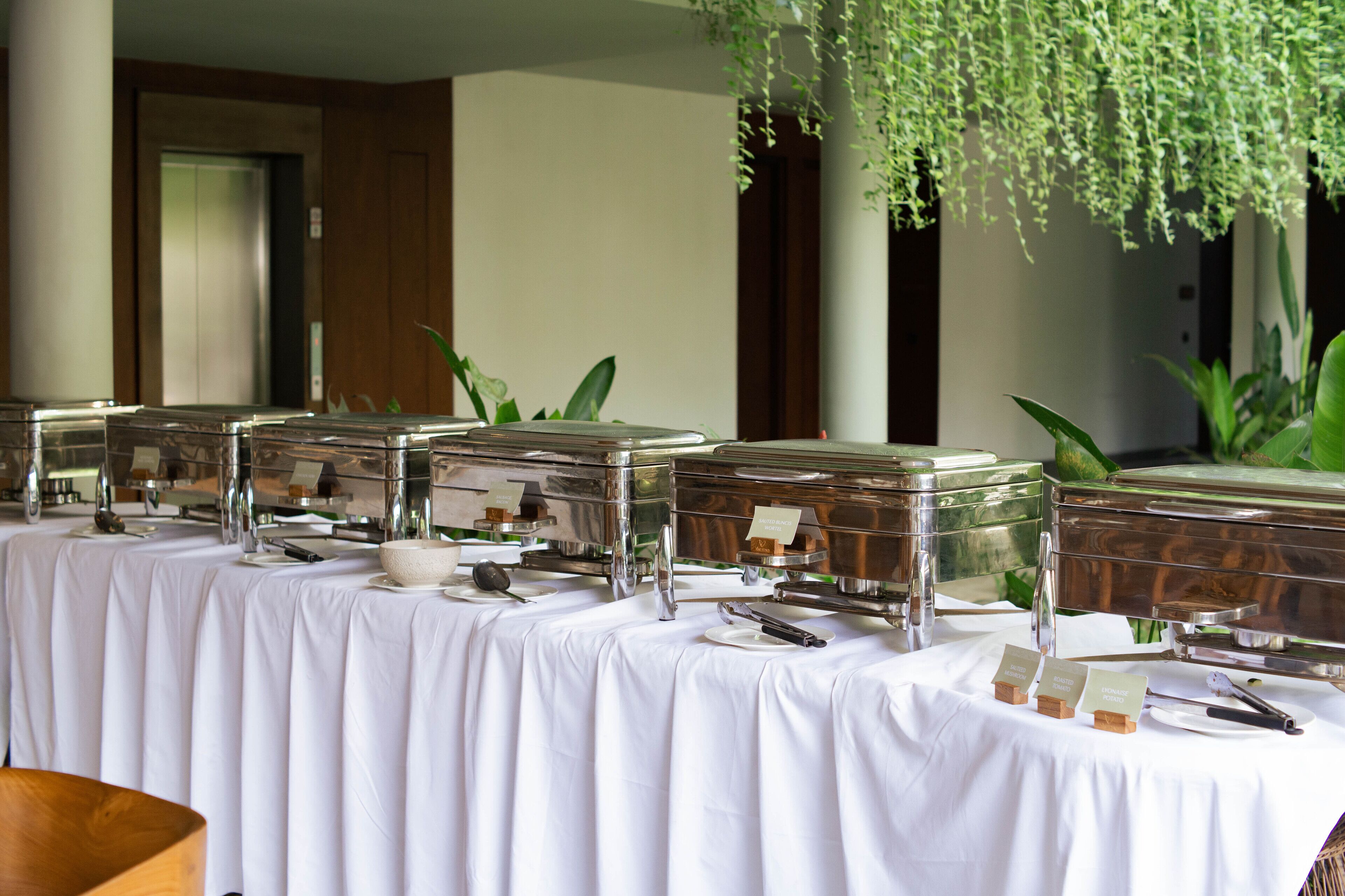 Ein Buffet mit mehreren Selbstbedienungsstationen, einer weißen Tischdecke und einer hängenden Pflanze.