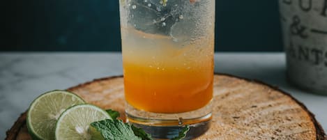 A tall glass of a citrus drink with lime and mint garnish, placed on a wooden slice.