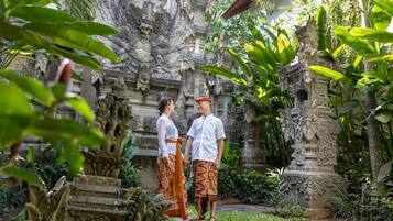 A couple standing in a garden with ornate stone carvings and tropical plants.