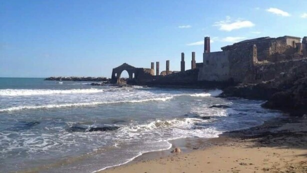 Una playa con olas, una estructura de piedra y un cielo despejado.