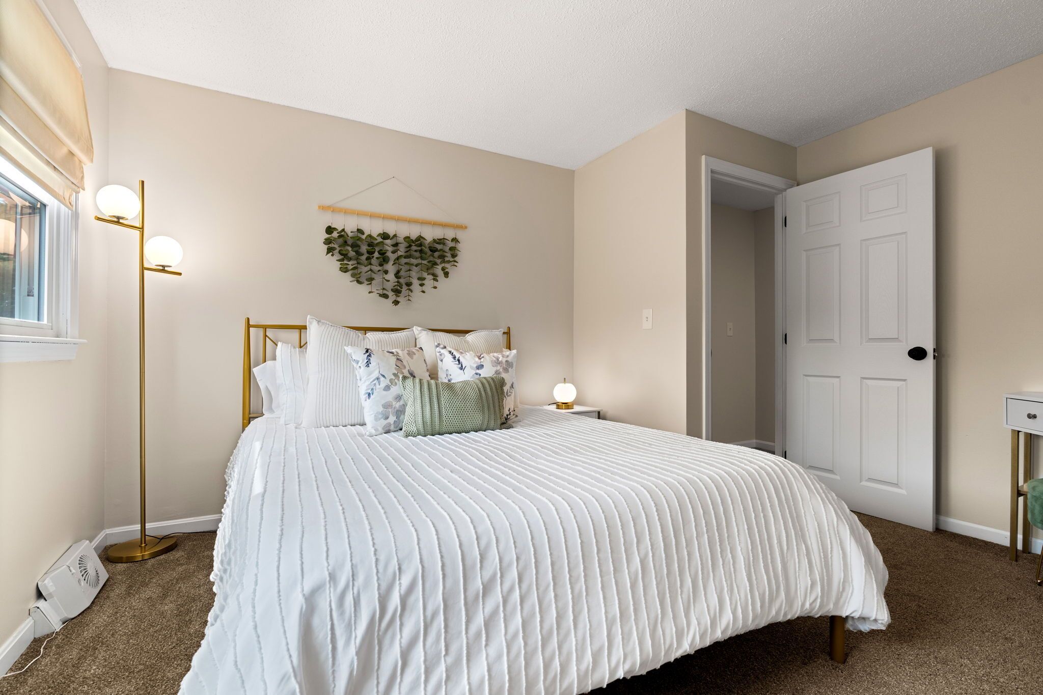 A bedroom with a bed, bedside lamps, a hanging plant, and a door.