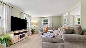A living room with a flat-screen TV, a grey sofa, a wooden entertainment unit, and a potted plant. - Beautiful & Relaxing Nashua Home - Minutes from Downtown (Nashua)