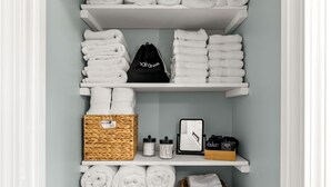 A neatly organized storage area with shelves holding rolled towels, a wicker basket, a small mirror, and a laundry basket. - Beautiful & Relaxing Nashua Home - Minutes from Downtown (Nashua)