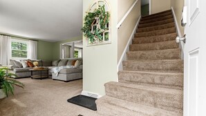 A living room with a staircase, a sofa set, and a decorative wall piece. - Beautiful & Relaxing Nashua Home - Minutes from Downtown (Nashua)