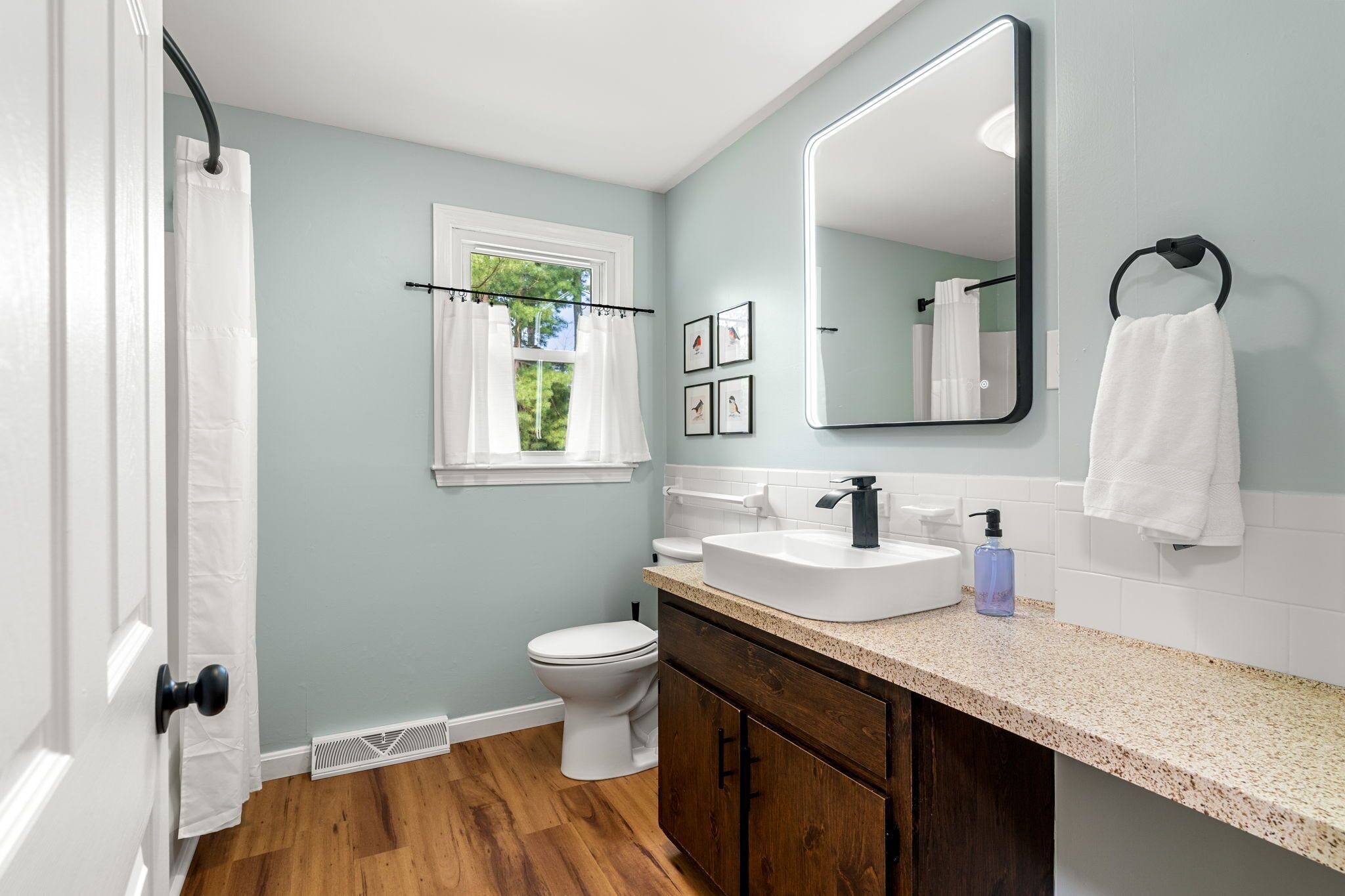 A bathroom with a white toilet, a sink with a mirror above it, and a window with a curtain.