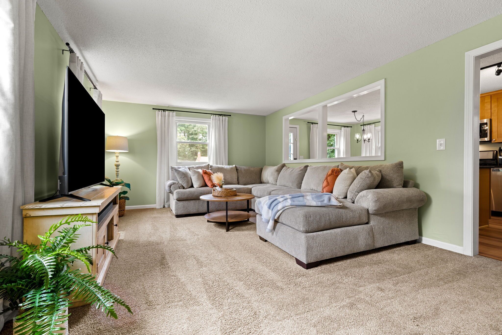 A living room with a sectional sofa, a coffee table, a TV stand, and a large mirror.