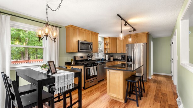 A modern kitchen with wooden cabinets, stainless steel appliances, and a dining area with a table and chairs. - Beautiful & Relaxing Nashua Home - Minutes from Downtown (Nashua)
