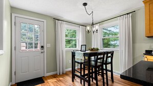 A dining area with a wooden table and chairs, a chandelier, and windows with white curtains. - Beautiful & Relaxing Nashua Home - Minutes from Downtown (Nashua)