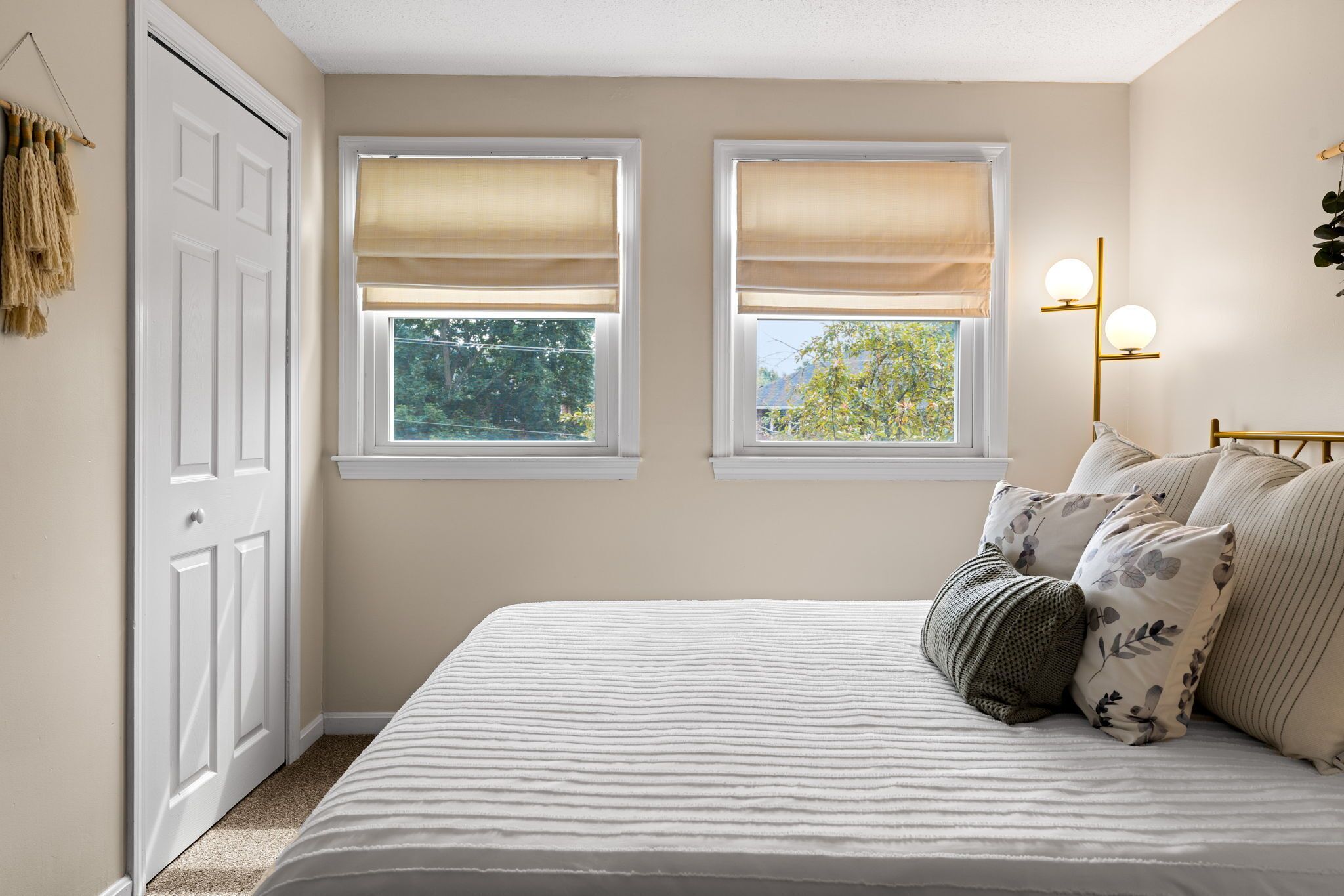 Un dormitorio con cama, dos ventanas con persianas, una puerta y un aplique de pared.
