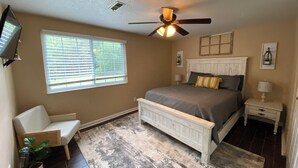 A bedroom with a bed, a ceiling fan, a window, a chair, and a nightstand.