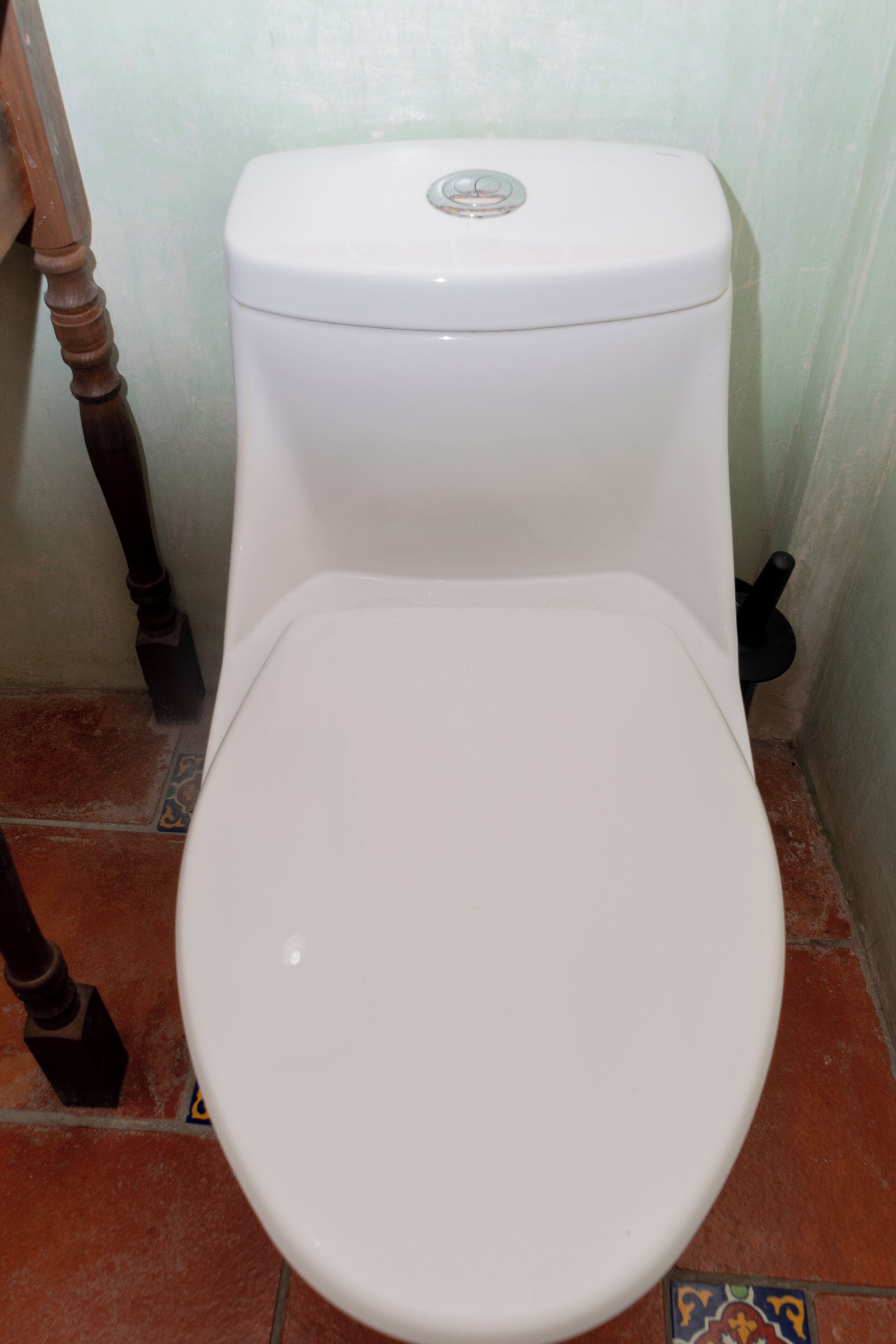 Valkoinen wc-istuin, jossa on pyöreä istuin ja huuhtelunappula päällä.