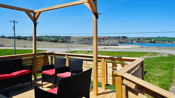 A wooden deck with outdoor furniture, a pergola, and a view of a lake and distant landscape. - Niseko Riverside by Zen Life : Greenie Cottage (New Glasgow)