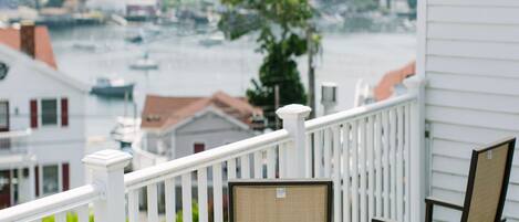 A balcony with white railings, two chairs, and a view of a lake with boats and buildings in the background.